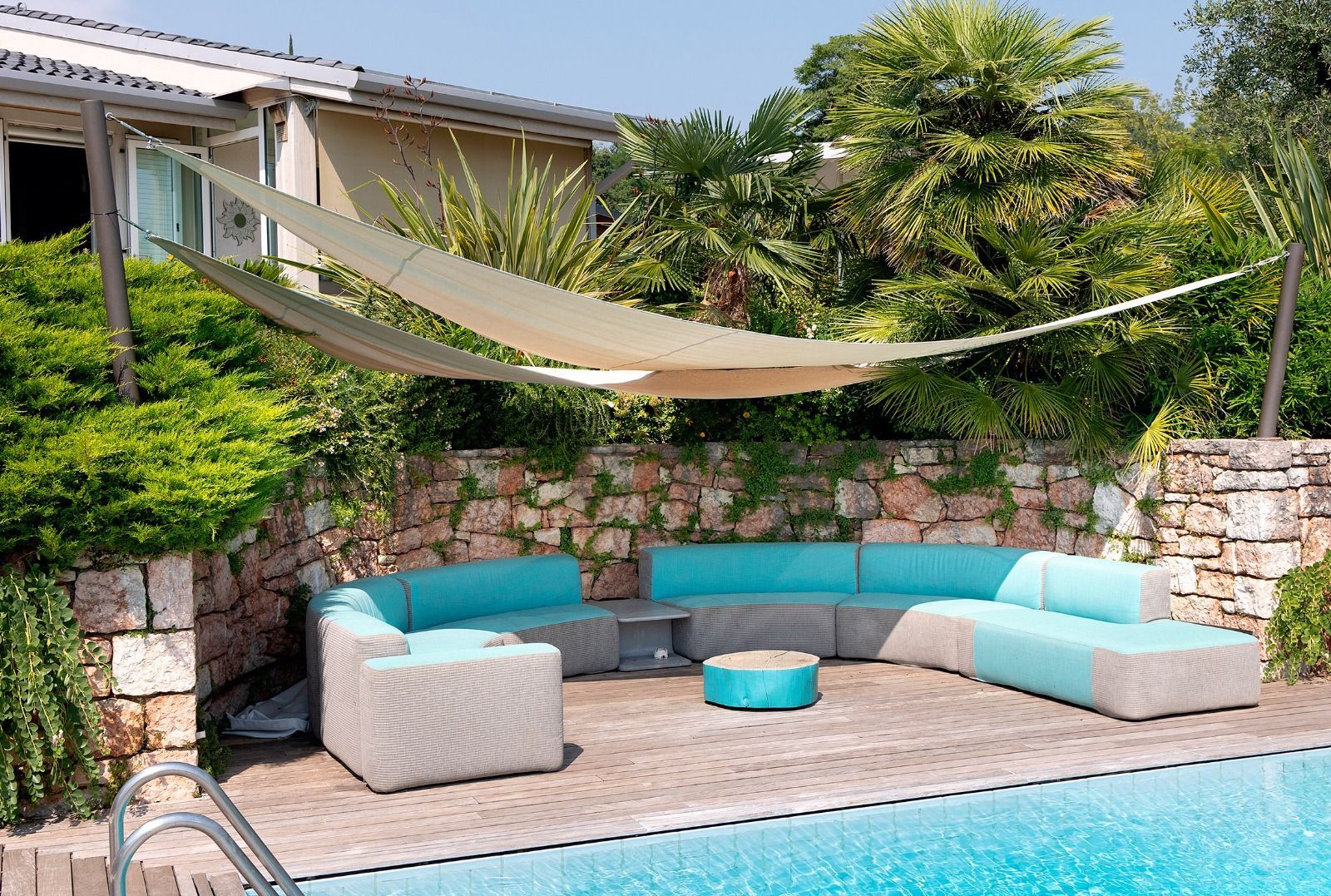 Patio con piscina sul retro, dotato di divani componibili turchesi, tettoia beige e pavimentazione in pietra.