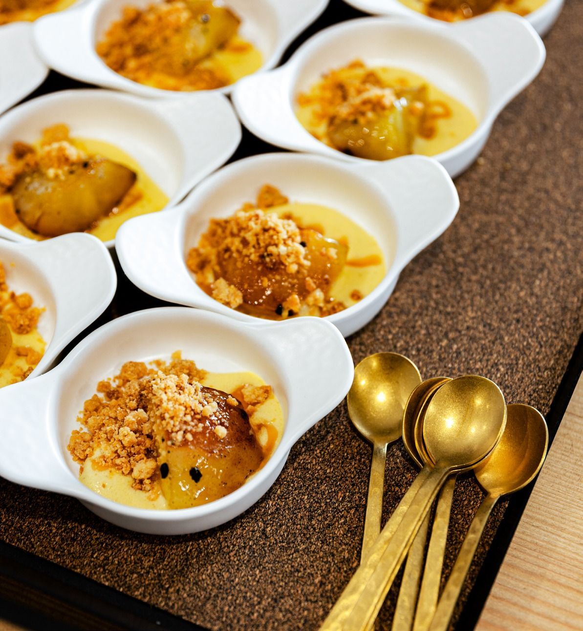 Piccoli cucchiaini bianchi di dessert guarniti con briciole, disposti su un tavolo accanto a cucchiaini dorati.