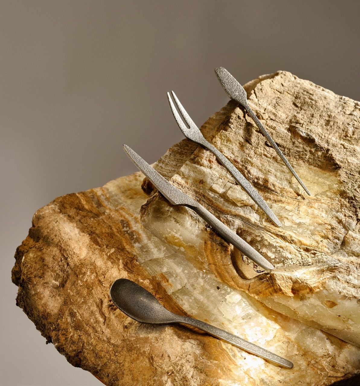 Una manciata di piccoli cucchiai d'argento poggiano su una superficie rocciosa stratificata di colore beige-marrone.