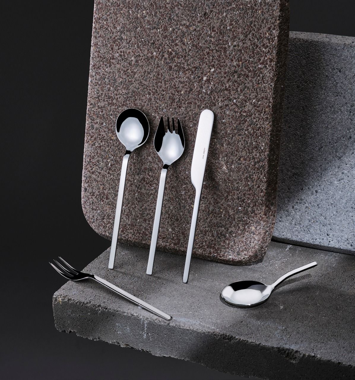 Cucchiai e utensili da cucina scultorei in argento su blocchi di schiuma scura, con manici bianchi e neri.