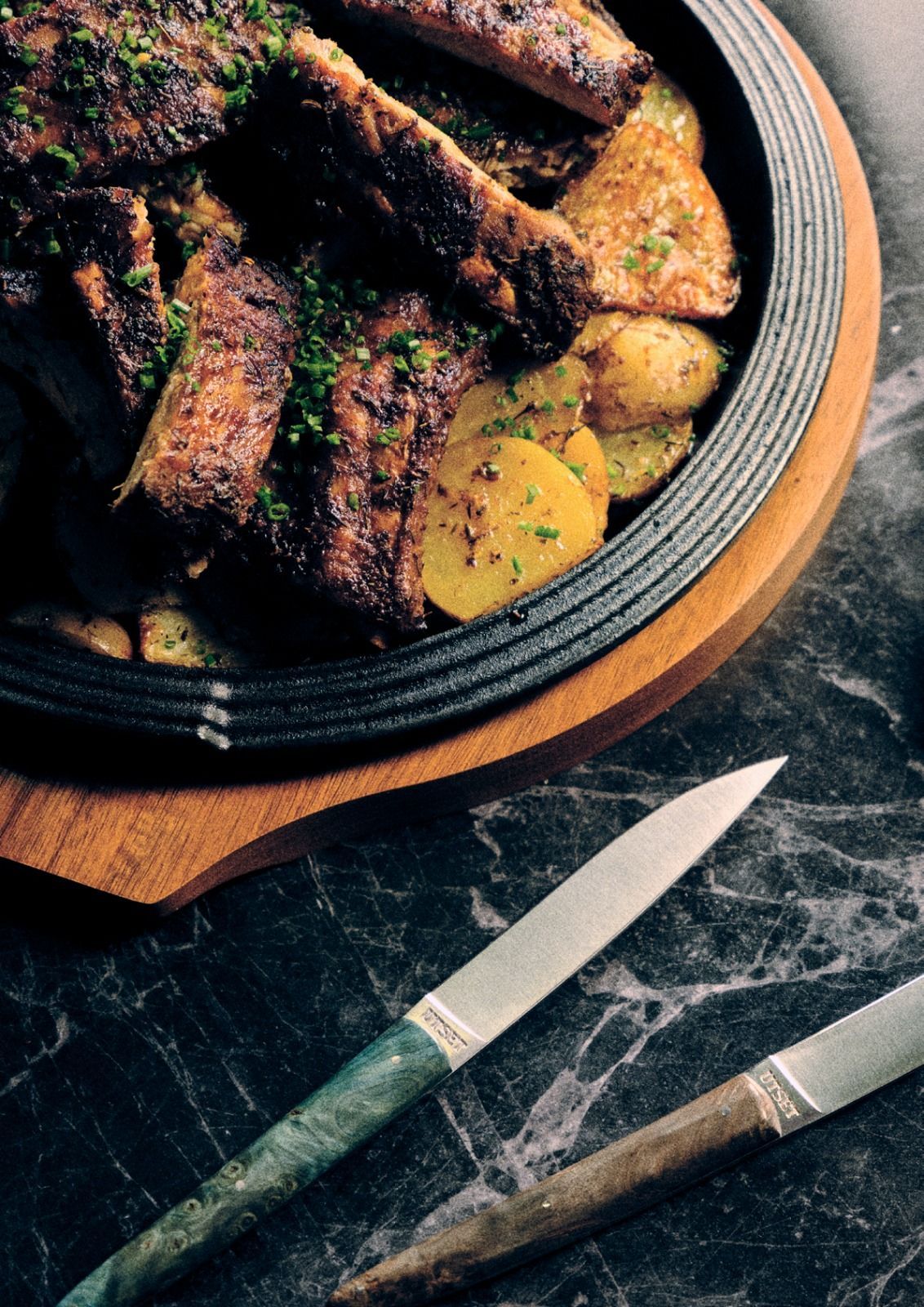 Bistecca grigliata e patate in una ciotola scura con un coltello su un tavolo di legno rustico