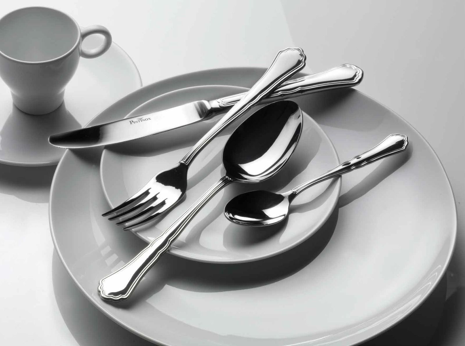 Servizio da tavola in bianco e nero con piatti, posate e una tazza su un piattino.