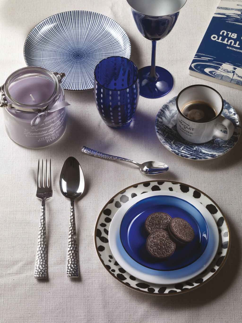 Tavola apparecchiata in blu e argento con bicchieri, piatti, posate e un piatto da dessert con biscotti.