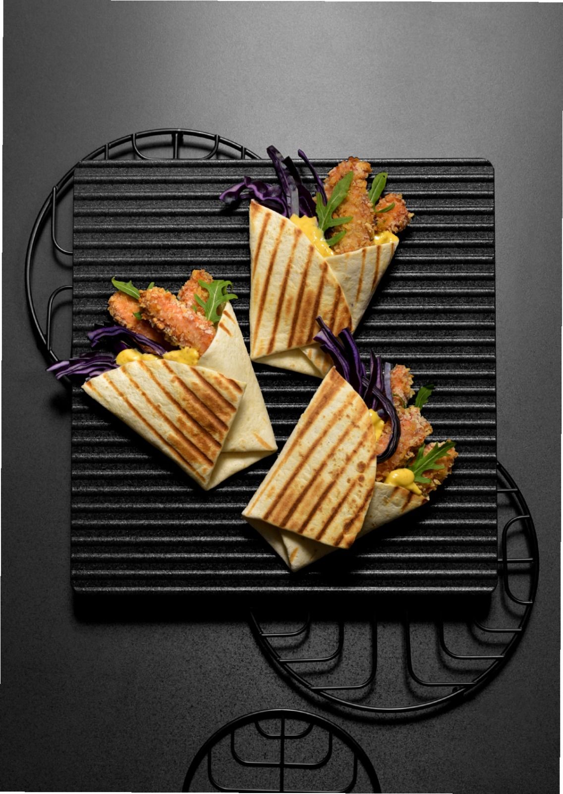 Tre piadine grigliate con verdure e patatine fritte su un vassoio nero testurizzato.