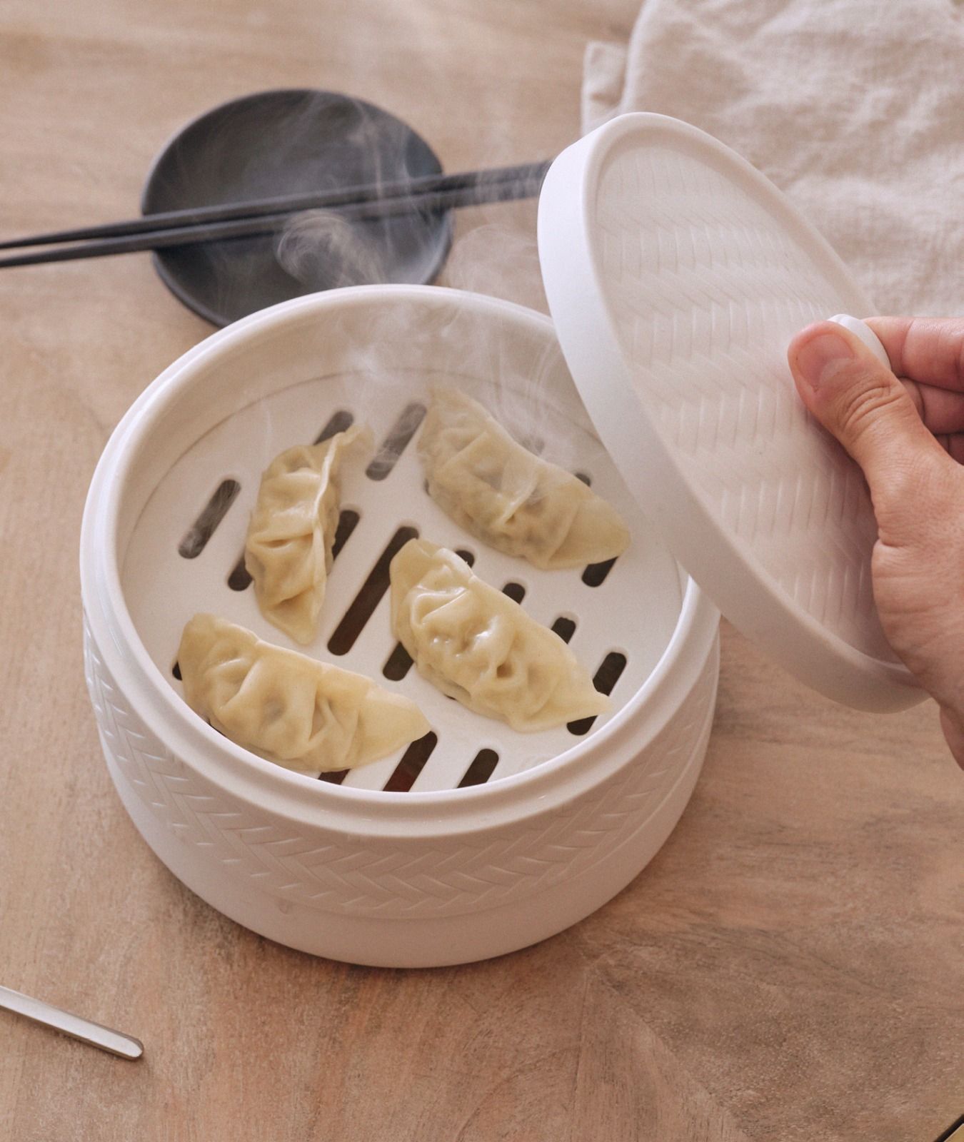 Ravioli al vapore in una vaporiera di bambù bianca, con una mano che solleva il coperchio