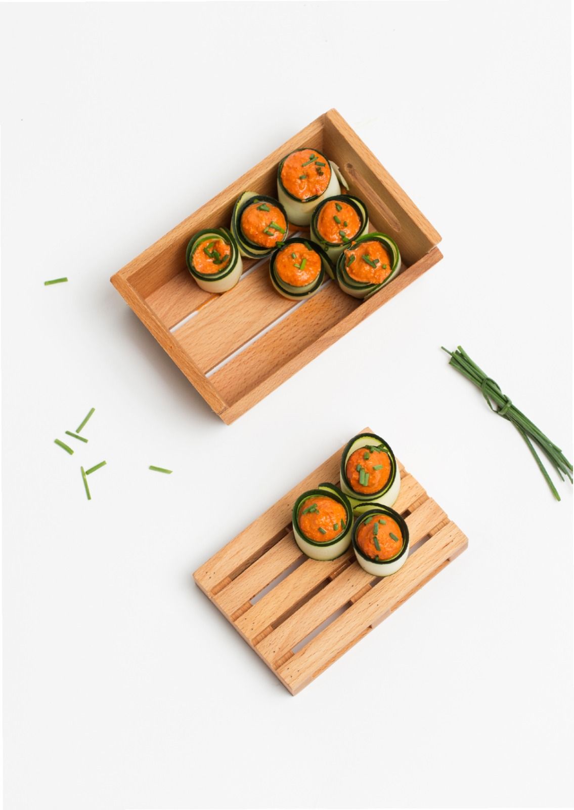 Due vassoi di legno con piccoli involtini di sushi e guarnizione verde su sfondo bianco.