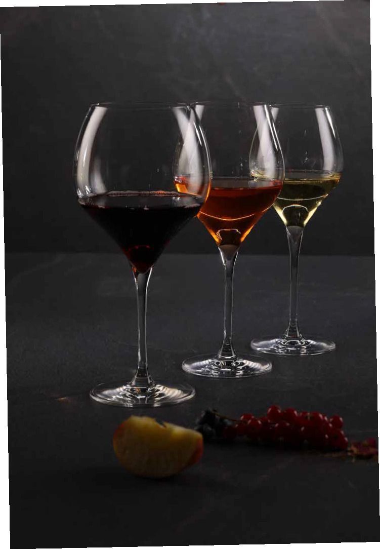 Tre calici di vino con vino rosso, ambrato e chiaro su un tavolo scuro, con frutta davanti.