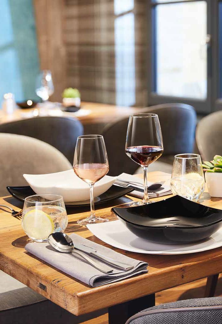 Elegante tavolo da ristorante apparecchiato con bicchieri da vino, tovaglioli piegati, ciotole e candele vicino a una finestra.