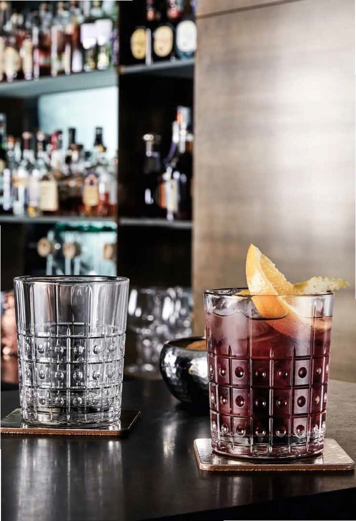 Due cocktail sul bancone del bar, uno rosso con guarnizione d'arancia accanto a un bicchiere da whisky vuoto.
