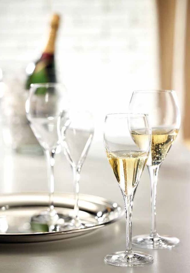 Calici da champagne su un vassoio accanto a una bottiglia ghiacciata, su una tavola apparecchiata con colori vivaci.