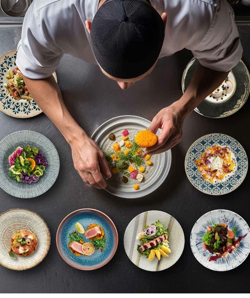Lo chef impiatta una colorata insalata gourmet su un tavolo scuro circondato da sei piccoli piatti.