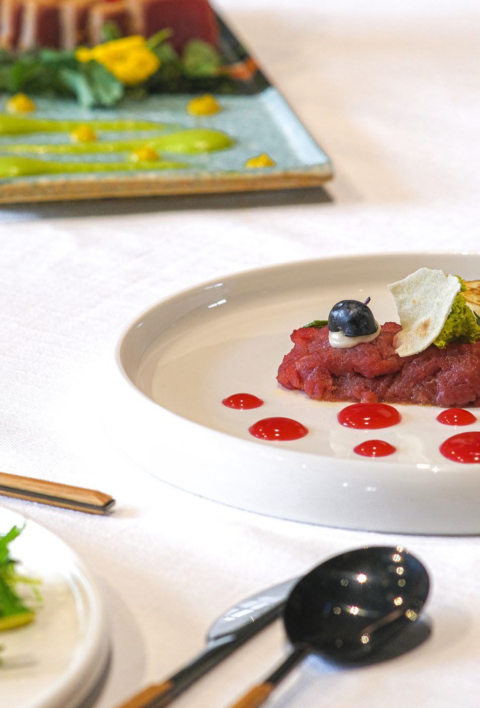 Elegante dessert impiattato su un piatto bianco con gocce di salsa rossa e un mirtillo su un tavolo