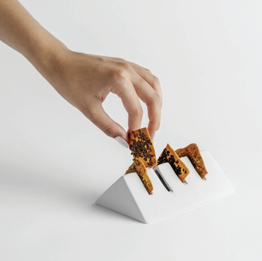 Mano che inserisce un biscotto ricoperto di cioccolato in un supporto geometrico bianco
