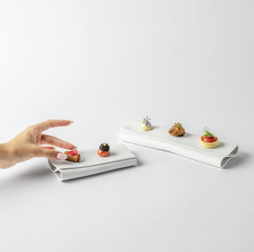Una mano posiziona un piccolo dessert su un vassoio bianco accanto a diverse piccole paste esposte.