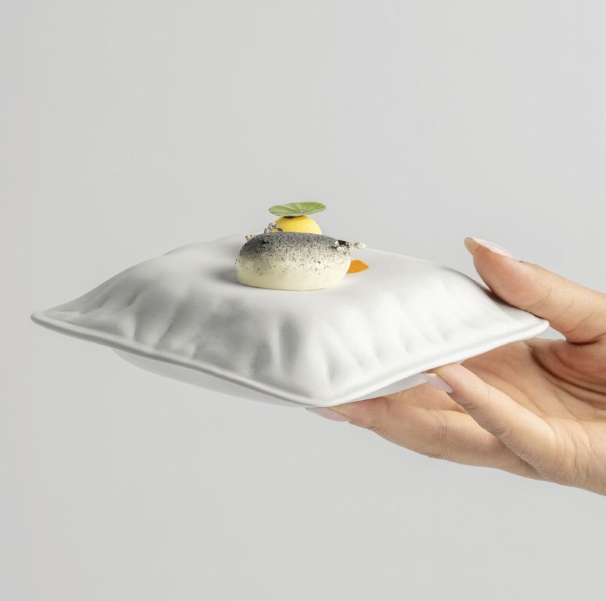 Mano che regge un vassoio bianco imbottito con un piccolo dessert guarnito con una decorazione verde.
