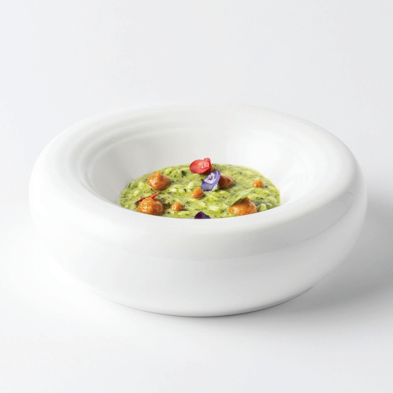 Ciotola di ceramica bianca con una piccola porzione di zuppa verde guarnita con decorazioni colorate.