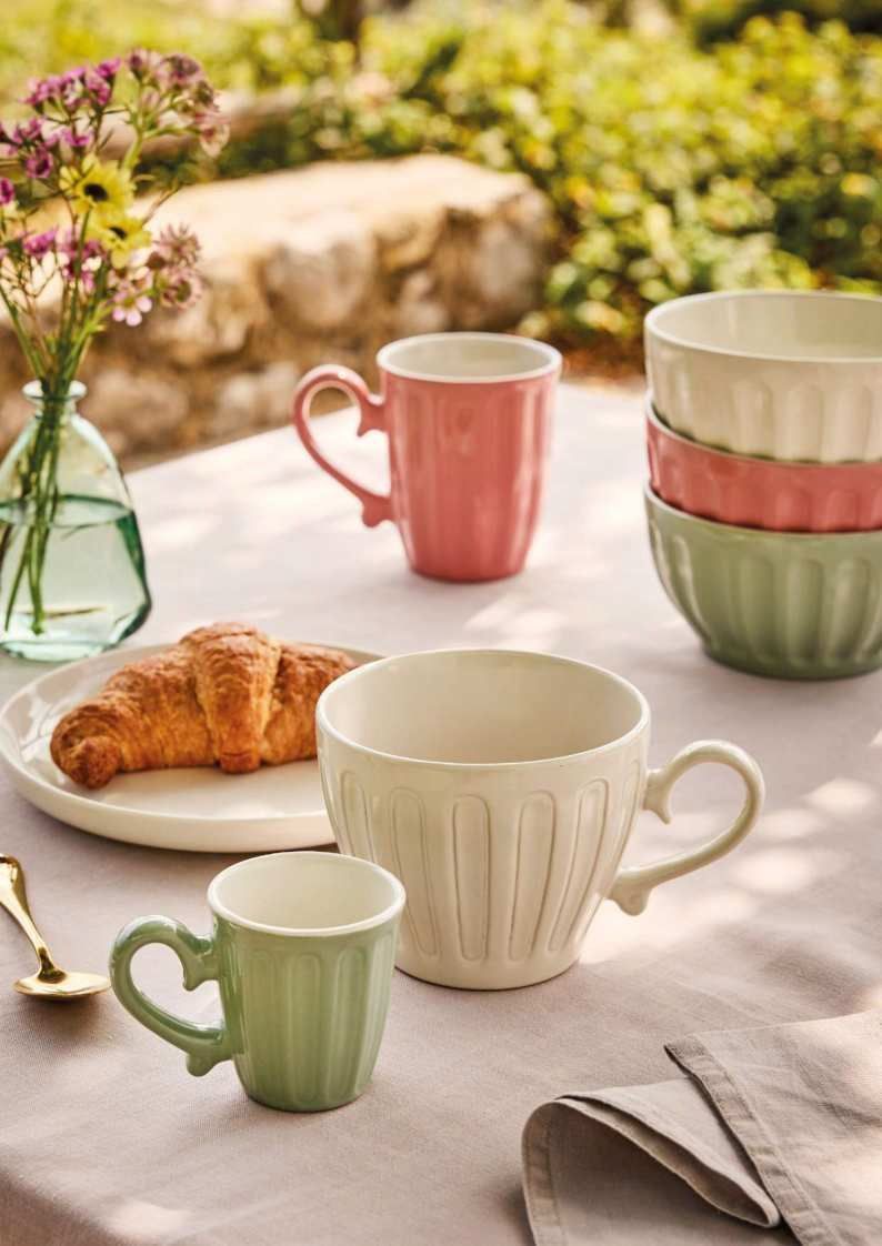 Tazze e tazzine dai colori pastello con un croissant su un tavolo da giardino.
