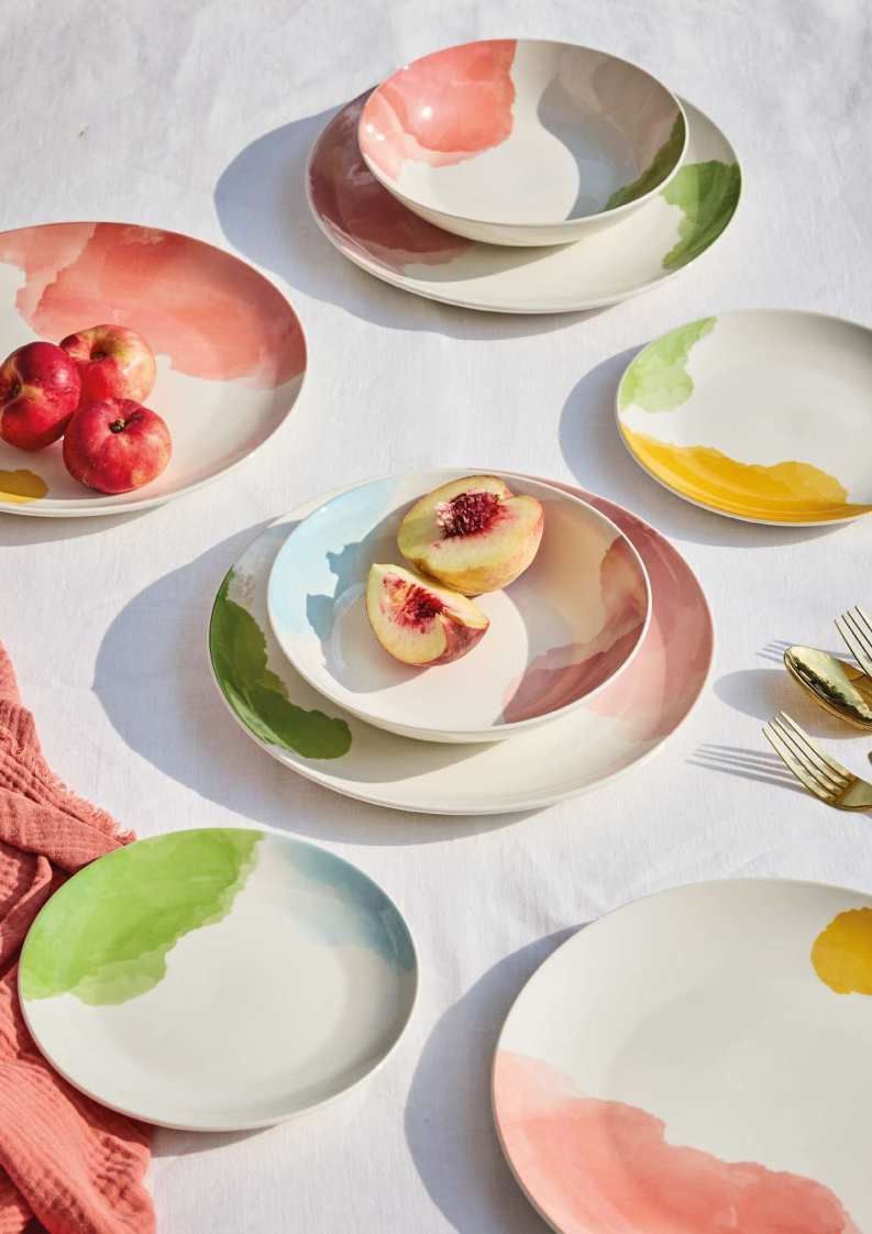 Piatti dai colori pastello con fette di pesca e frutti di bosco su una tovaglia bianca.