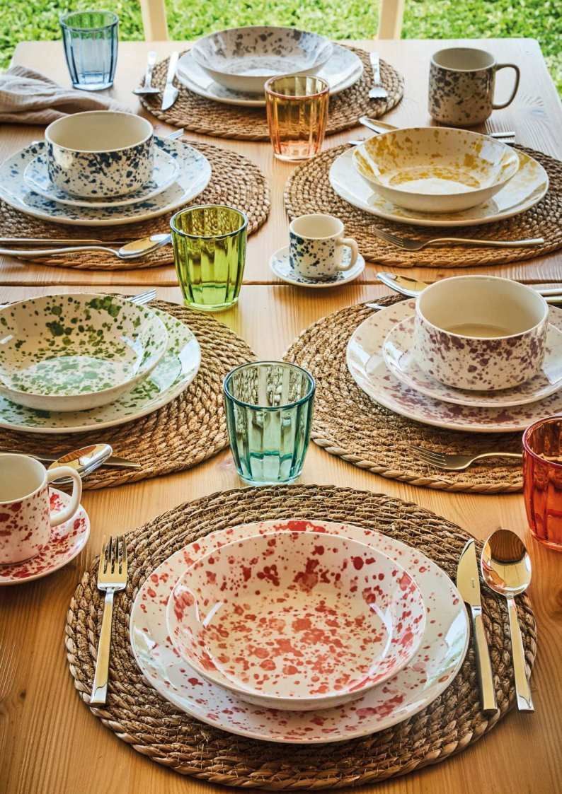 Elegante set da tavola con piatti decorati, tovagliette intrecciate e bicchieri colorati per un pasto