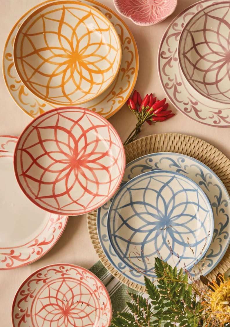 Piatti in ceramica colorati e decorati con fiori secchi e verde su sfondo beige.