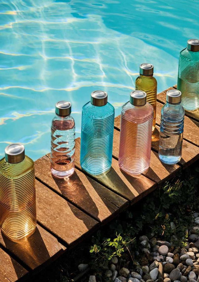 Bottiglie di vetro colorate allineate su una sporgenza a bordo piscina, accanto all'acqua blu brillante.