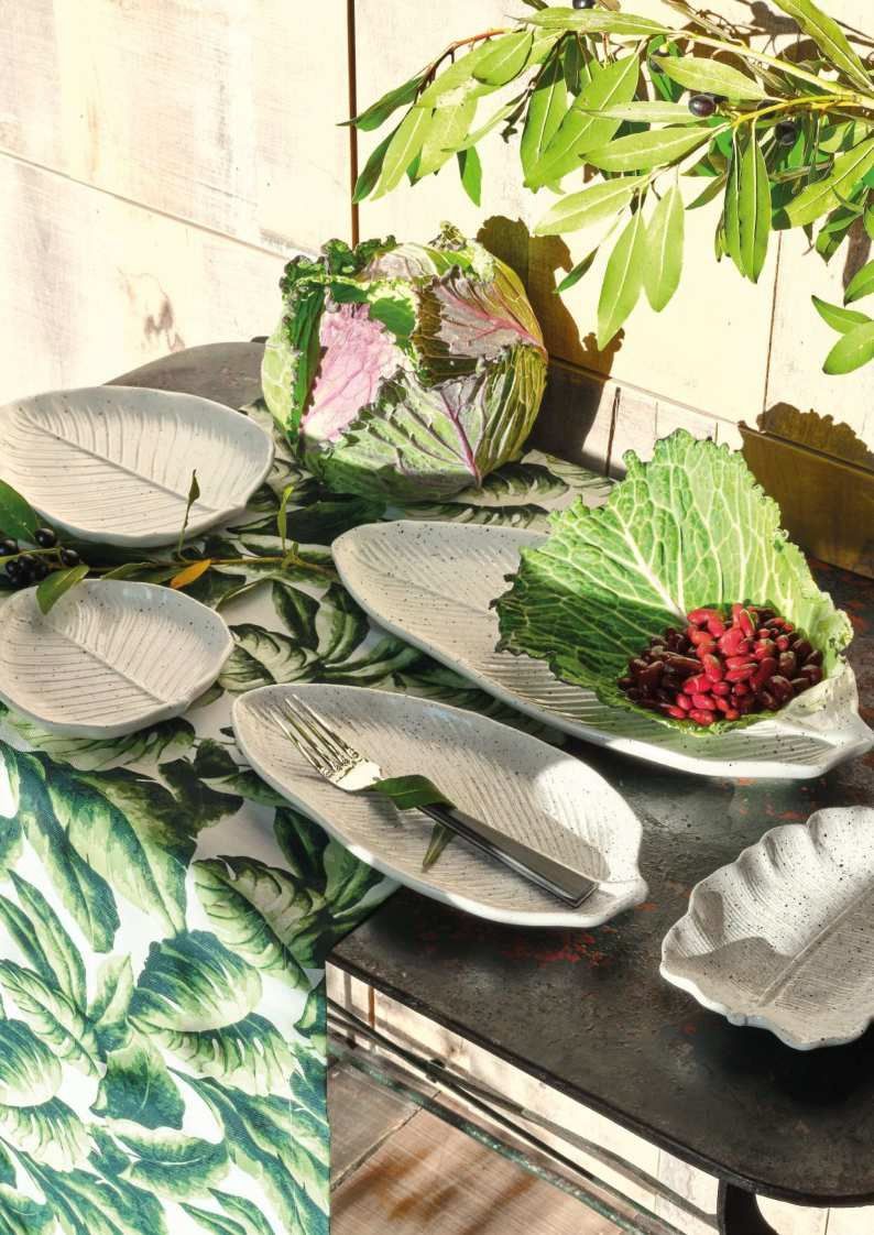 Piatti decorativi in ceramica con foglie verdi e fiori rosa su un tavolo, con rami frondosi sopra.