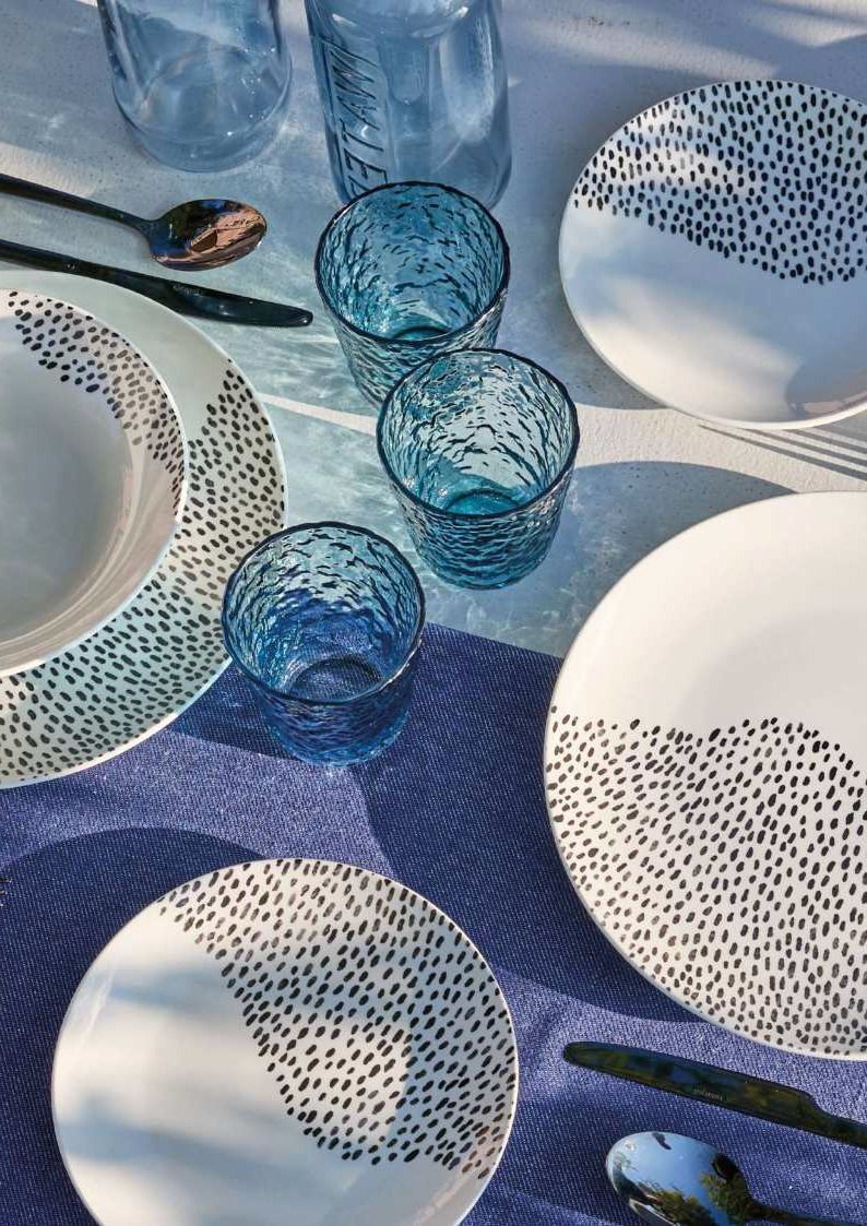 Piatti in vetro blu e ceramica a pois bianchi disposti su una tavola apparecchiata in blu e bianco.