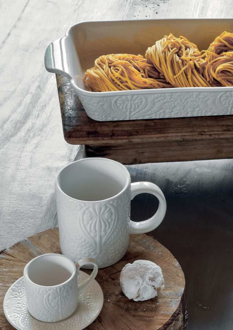 Tazze bianche e un piattino su un tavolo di legno, accanto a un vassoio di pasticcini su una tovaglia bianca.