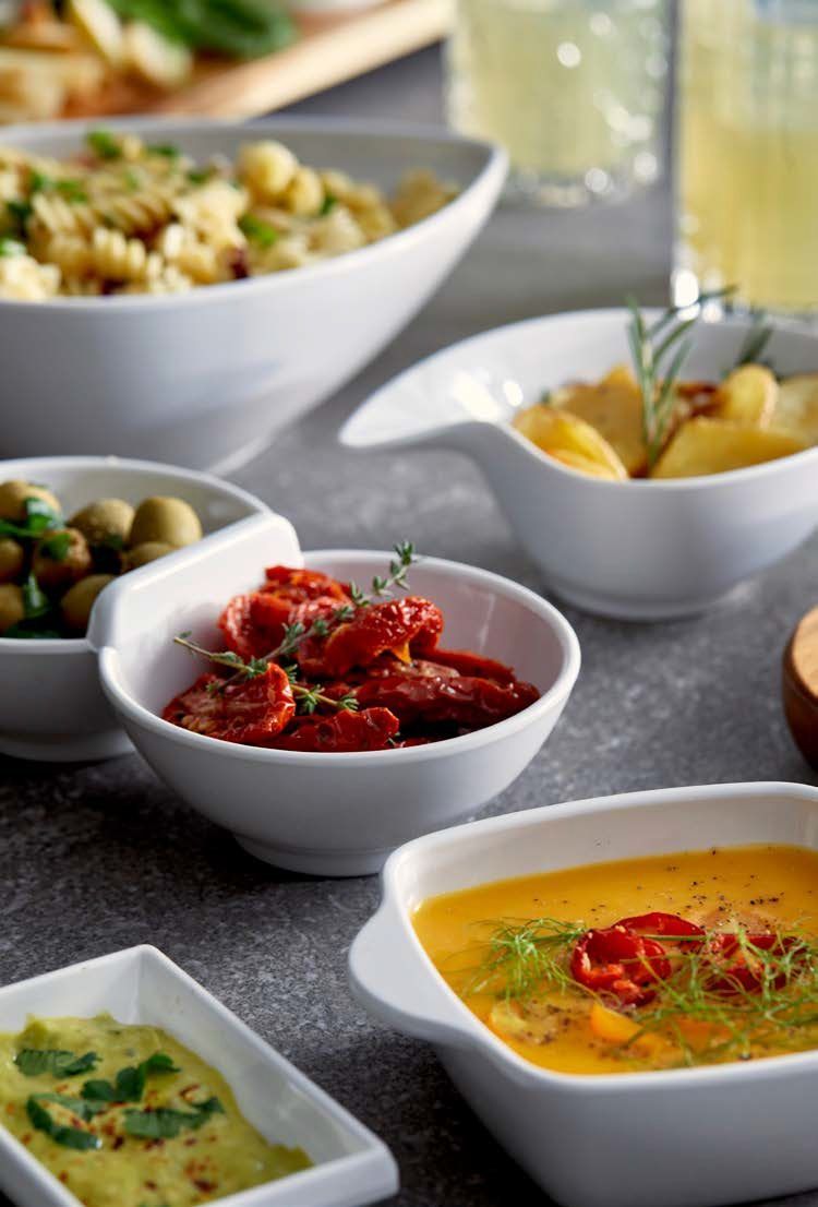 Antipasti assortiti e colorati in ciotole bianche su un tavolo da pranzo, tra cui zuppa di pomodoro rossa, zuppa gialla e salsa verde.