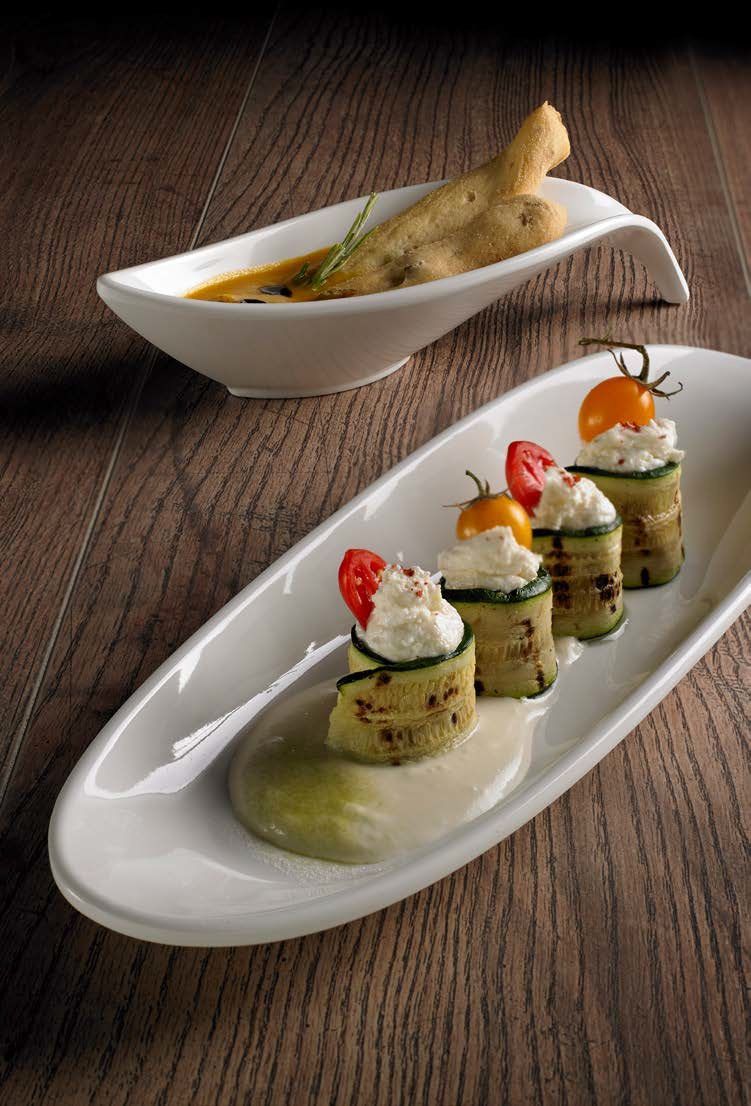 Involtini gourmet da antipasto su piatti bianchi con guarnizioni colorate e salse di accompagnamento su un tavolo di legno.