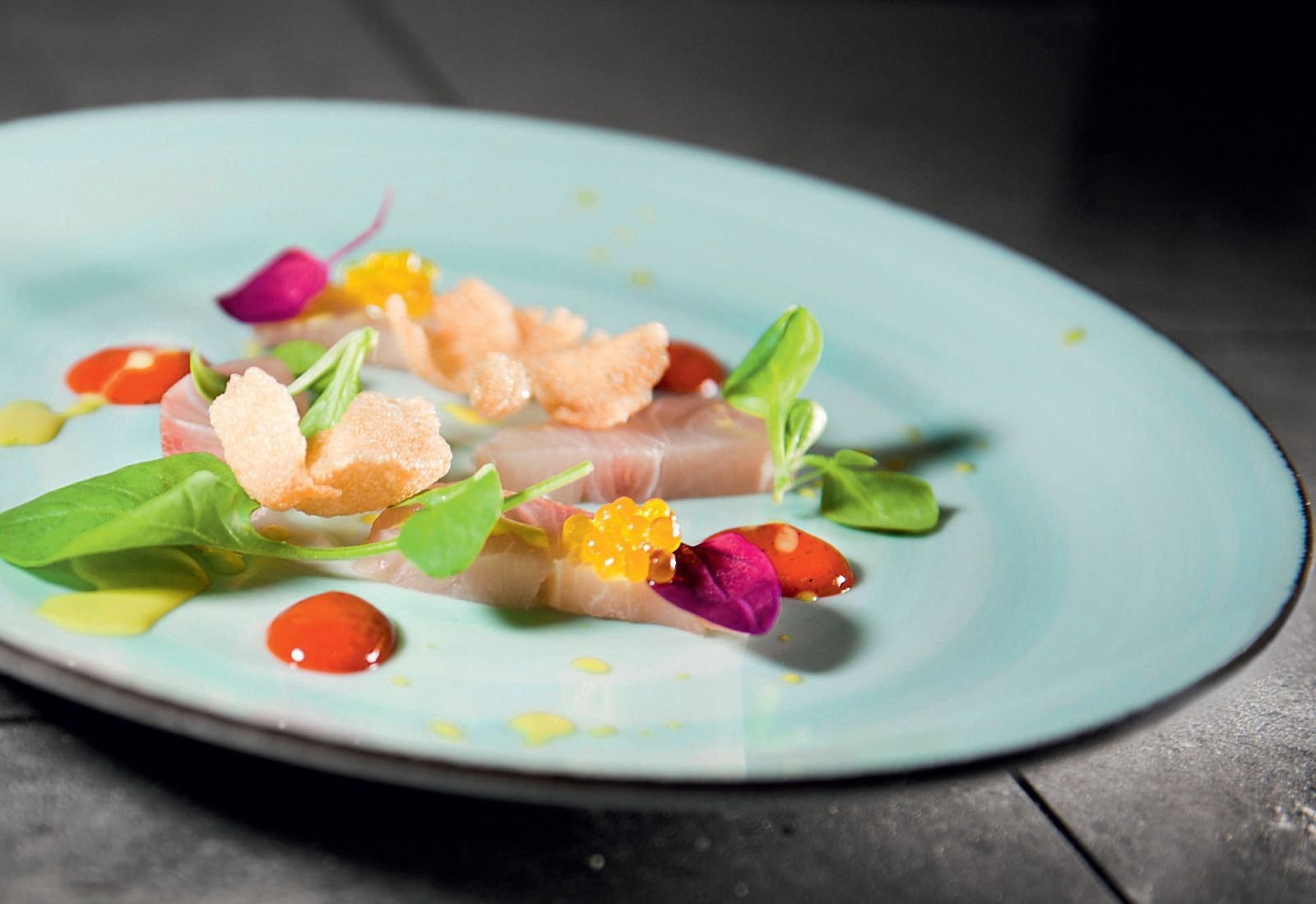 Insalata gourmet impiattata con verdure, fiori rosa e salmone su un piatto blu.