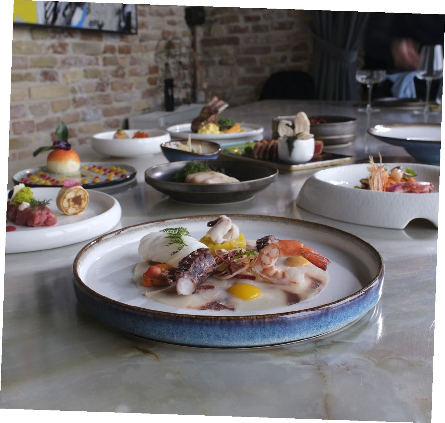 Piatti gourmet a base di pesce disposti su un tavolo di ristorante, con uno sfondo di un rustico muro di mattoni.