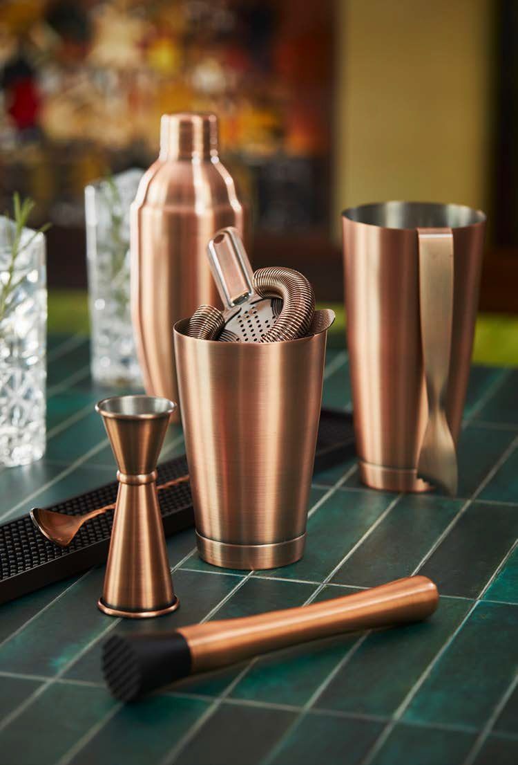 Set da cocktail in rame con misurino, colino, pestello e bicchiere da miscelazione, su un tappetino da bar.