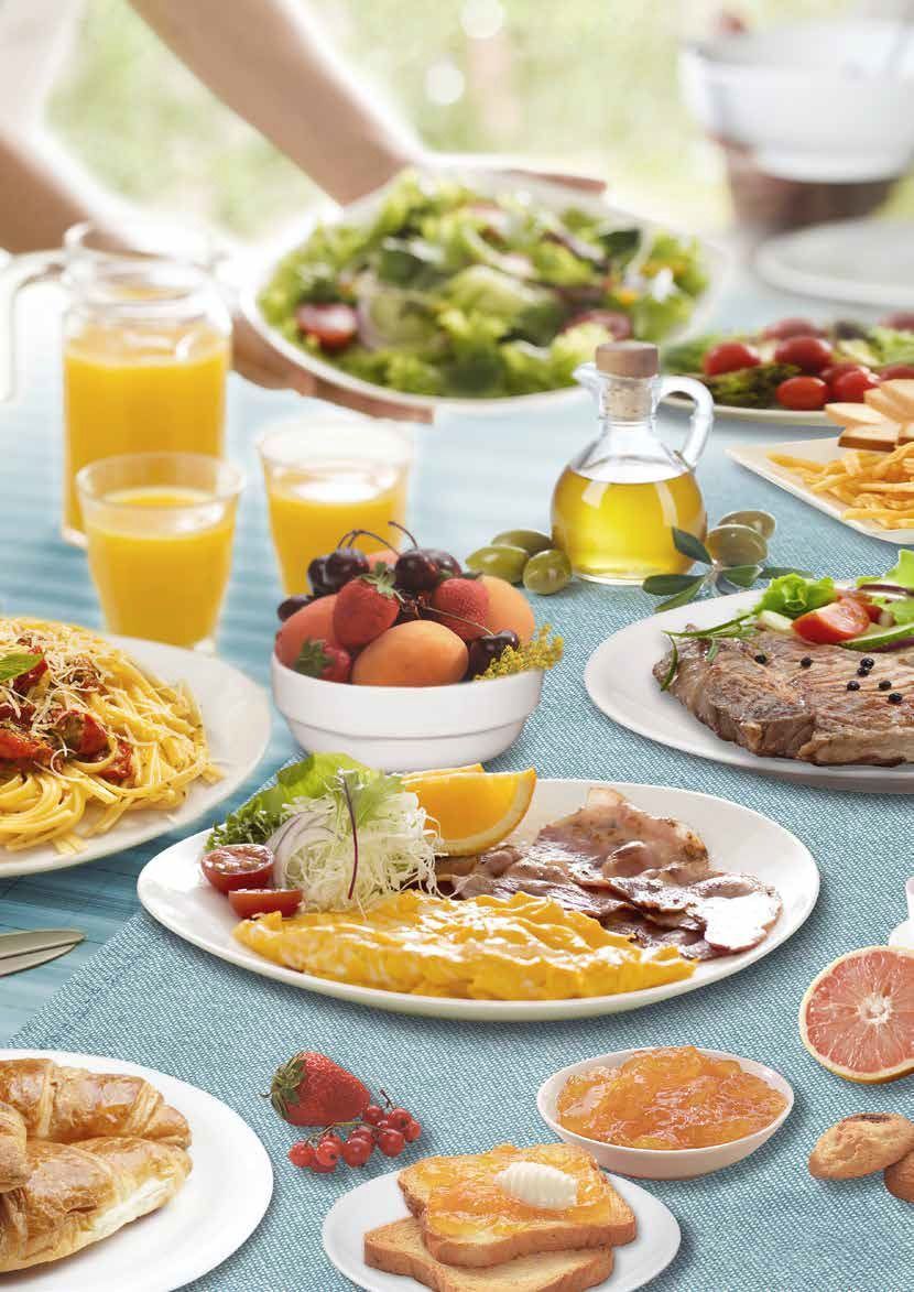 Tavolo da brunch con succo d'arancia, frutta, uova, pasticcini, caffè e carne alla griglia serviti su piatti