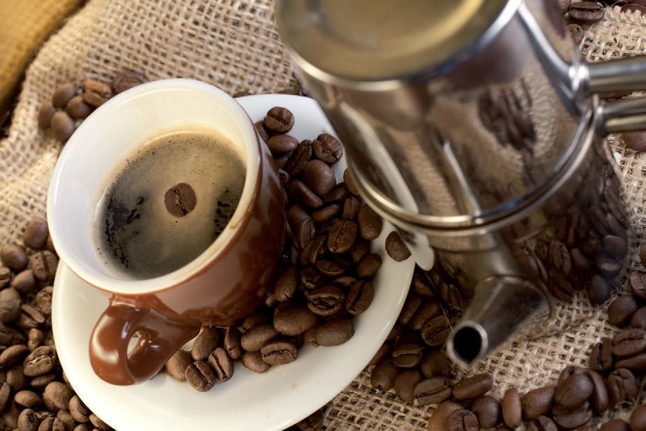 Tazza di caffè con chicchi rovesciati accanto a un macinacaffè di metallo su un telo di iuta.