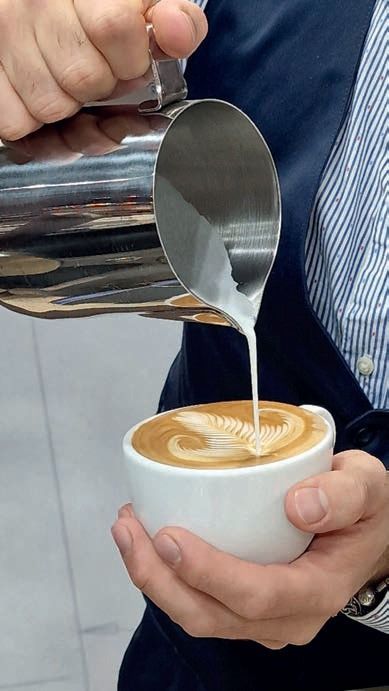 Il latte viene versato da una brocca di metallo in una tazza bianca di caffè latte art.