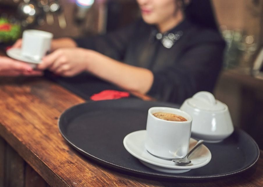 Tazze da caffè su un vassoio in un bar, con una persona che tiene una tazza sullo sfondo.