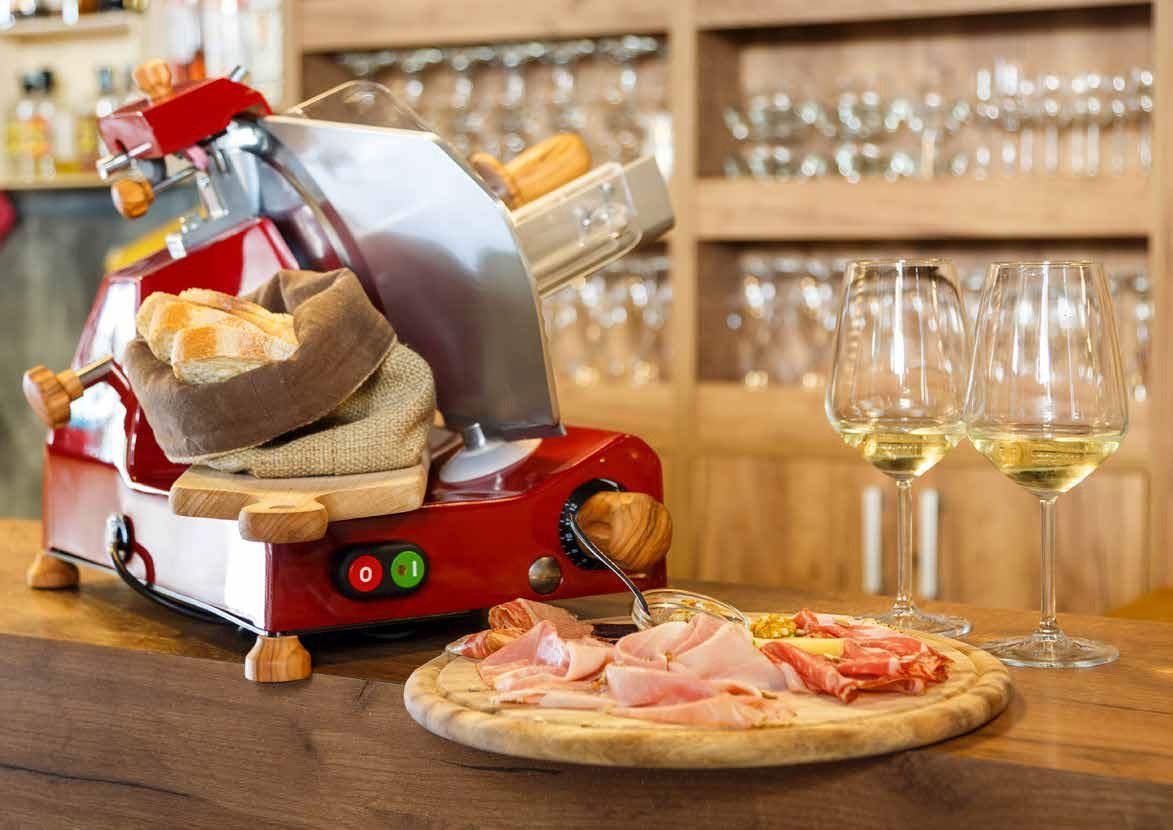 Pentola per fonduta di formaggio con pane, salumi e bicchieri da vino su un tavolo di legno in un'accogliente atmosfera da bar.