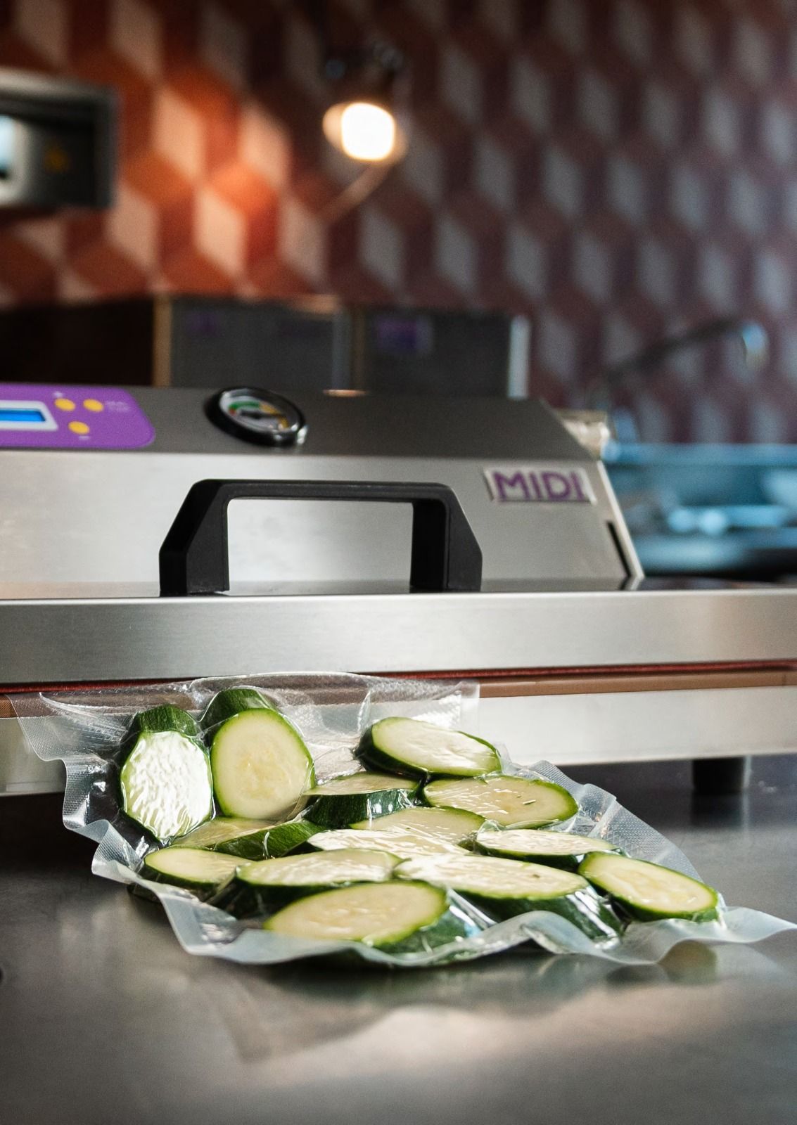 Zucchine affettate che fuoriescono da una macchina per la lavorazione delle verdure e si riversano su un vassoio di metallo.