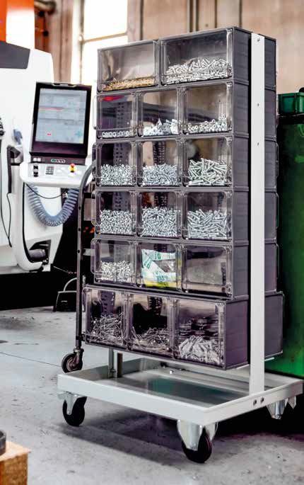 Armadio metallico con numerosi contenitori etichettati su un carrello con ruote, accanto a un chiosco touchscreen in un laboratorio o in un'officina.