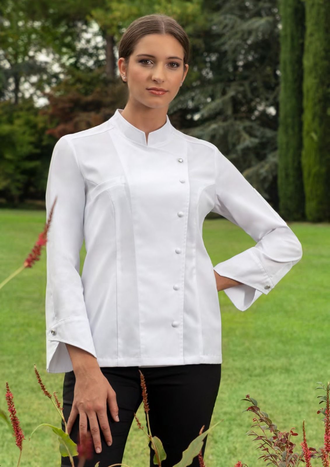 Una donna con una giacca da chef bianca è in piedi in un giardino con piante e fiori rossi.
