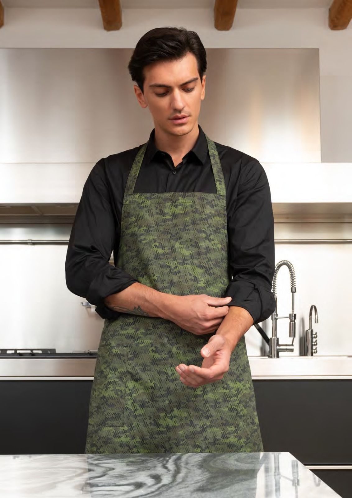 In una cucina moderna, una persona con un grembiule verde si rimbocca una manica nera.