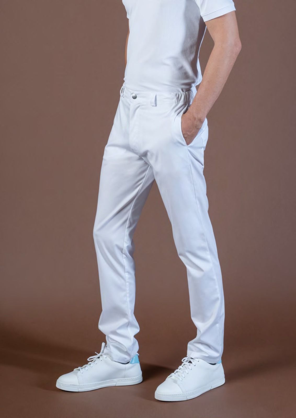 Persona che indossa pantaloni bianchi, camicia bianca e scarpe da ginnastica bianche su sfondo marrone.