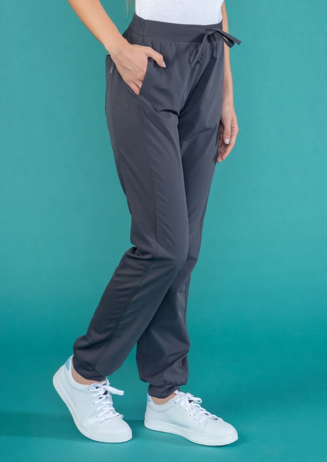 Persona che indossa pantaloni della tuta grigi e scarpe da ginnastica bianche su sfondo verde acqua.