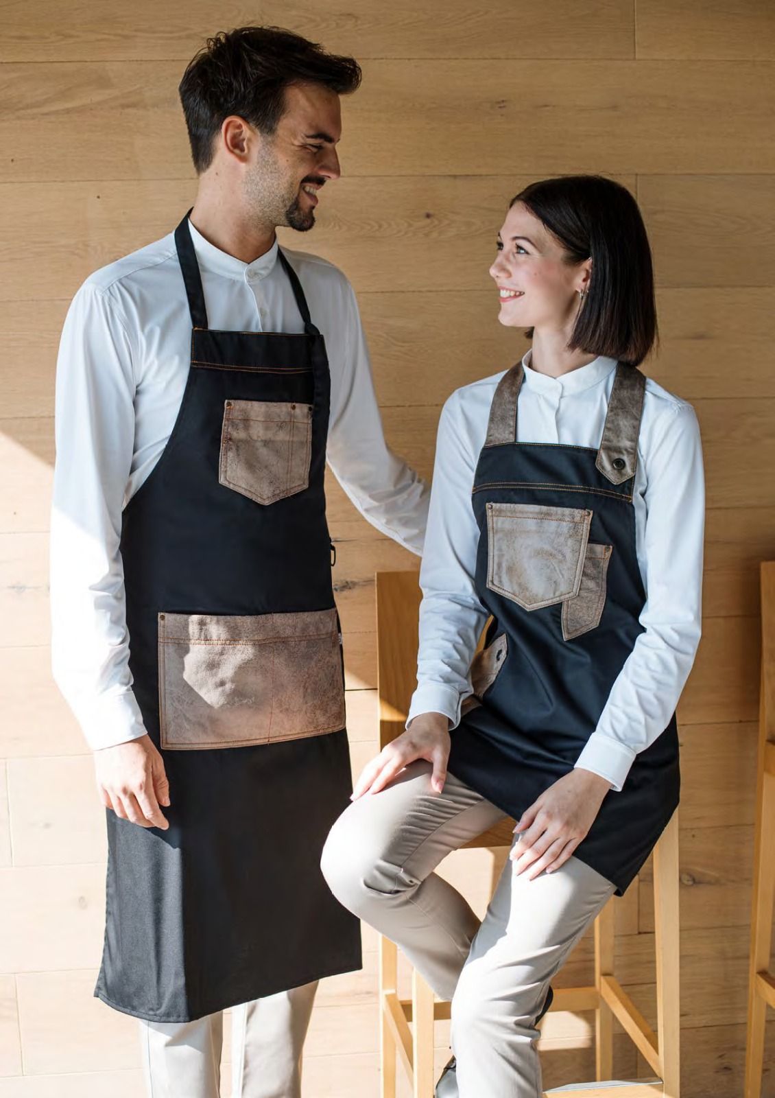Due persone con indosso un grembiule sono in piedi e sedute in cucina, sorridendosi a vicenda.