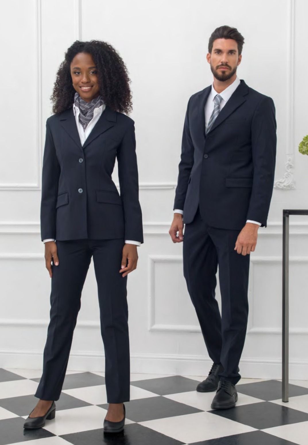 Due professionisti in abiti blu scuro in piedi in un ufficio luminoso con pavimento a scacchi bianchi e neri.