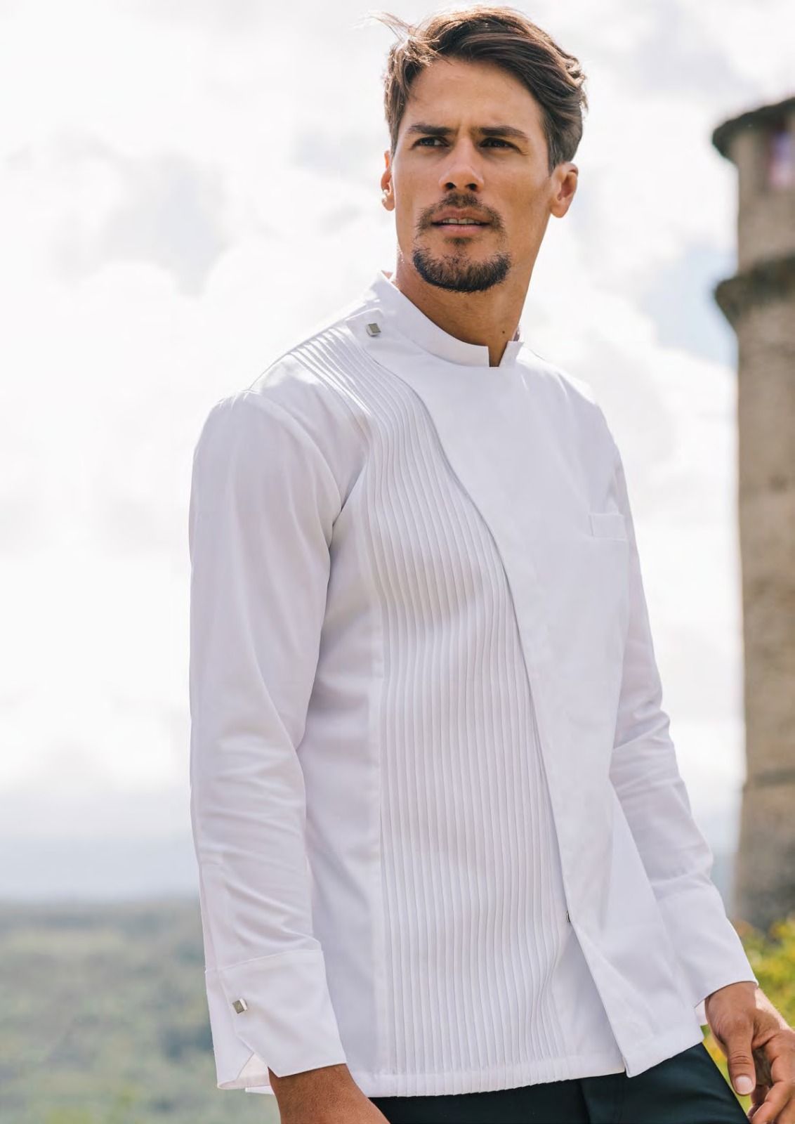 Un uomo con una camicia bianca abbottonata è in piedi all'aperto e guarda di lato.