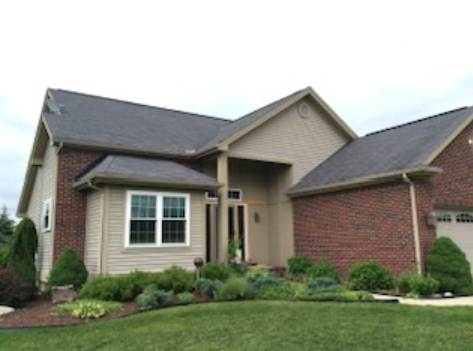 Suburban brick house with beige siding, bay window, and green lawn under a cloudy sky
