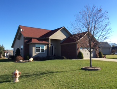 Suburban house with red roof, front lawn, young tree, and fire hydrant under a clear blue sky