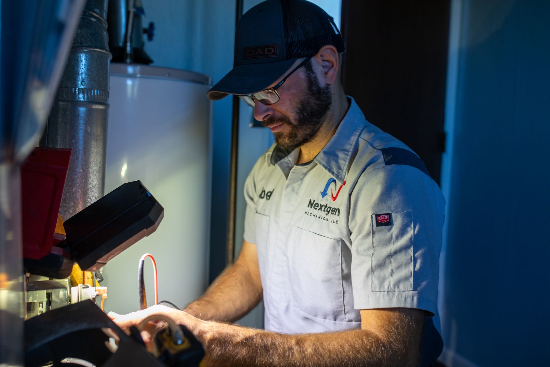 Plumber in uniform inspecting a water heater, using a flashlight.